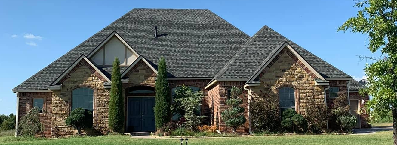 Brick suburban house with a dark shingled roof, arched entryway, and landscaped front yard