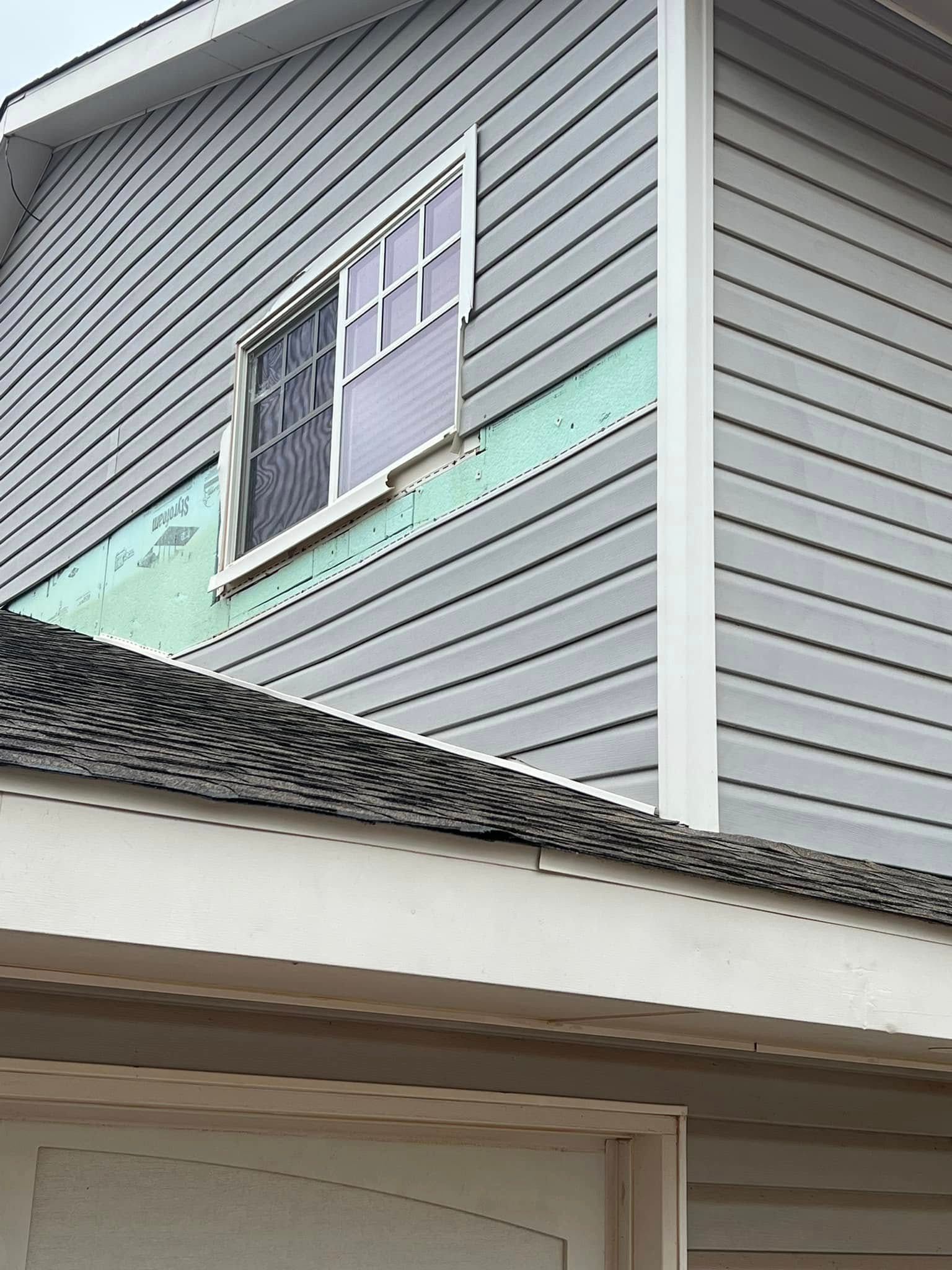 Broken second-story window on a gray house exterior with green trim and roofline below