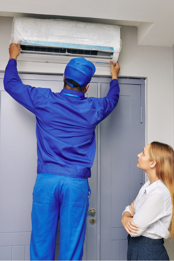 A man is installing an air conditioner while a woman looks on.