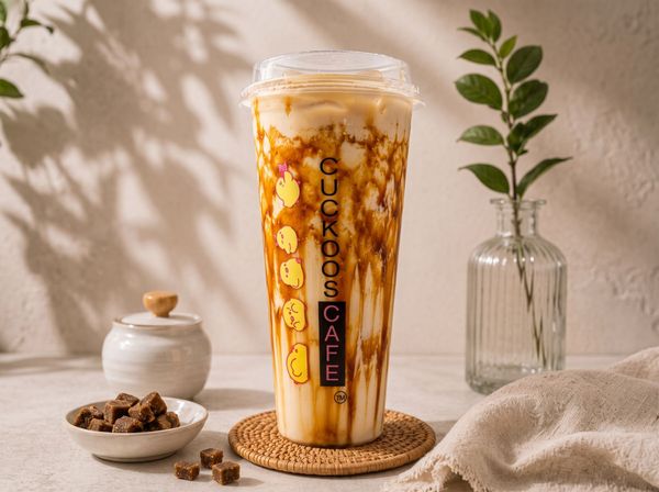 Iced caramel coffee in a clear cup on a woven coaster with a plant and ceramic bowl on a beige surface