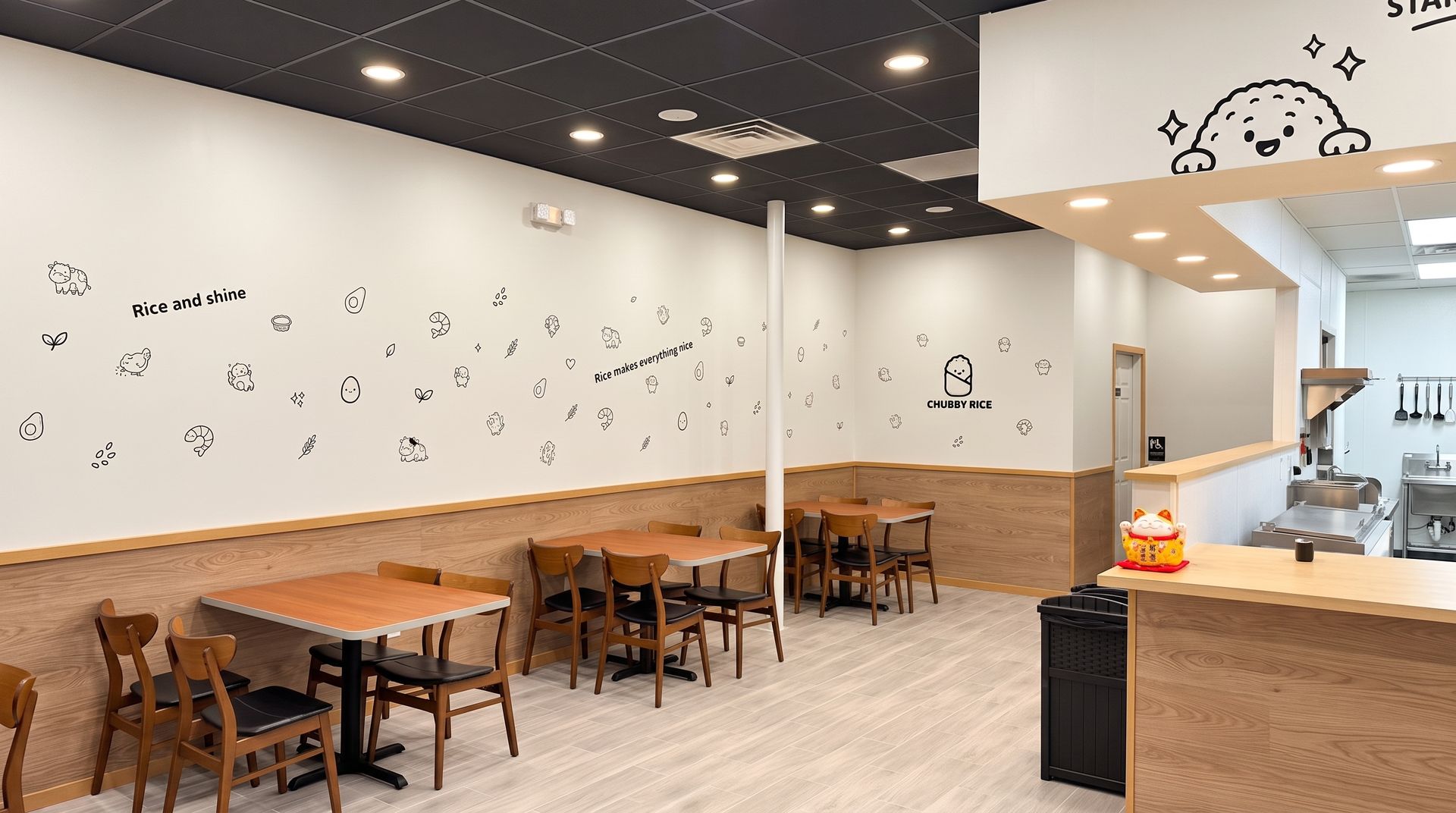 Empty café with wooden tables, tan chairs, white walls with doodles, and a counter area on the right.