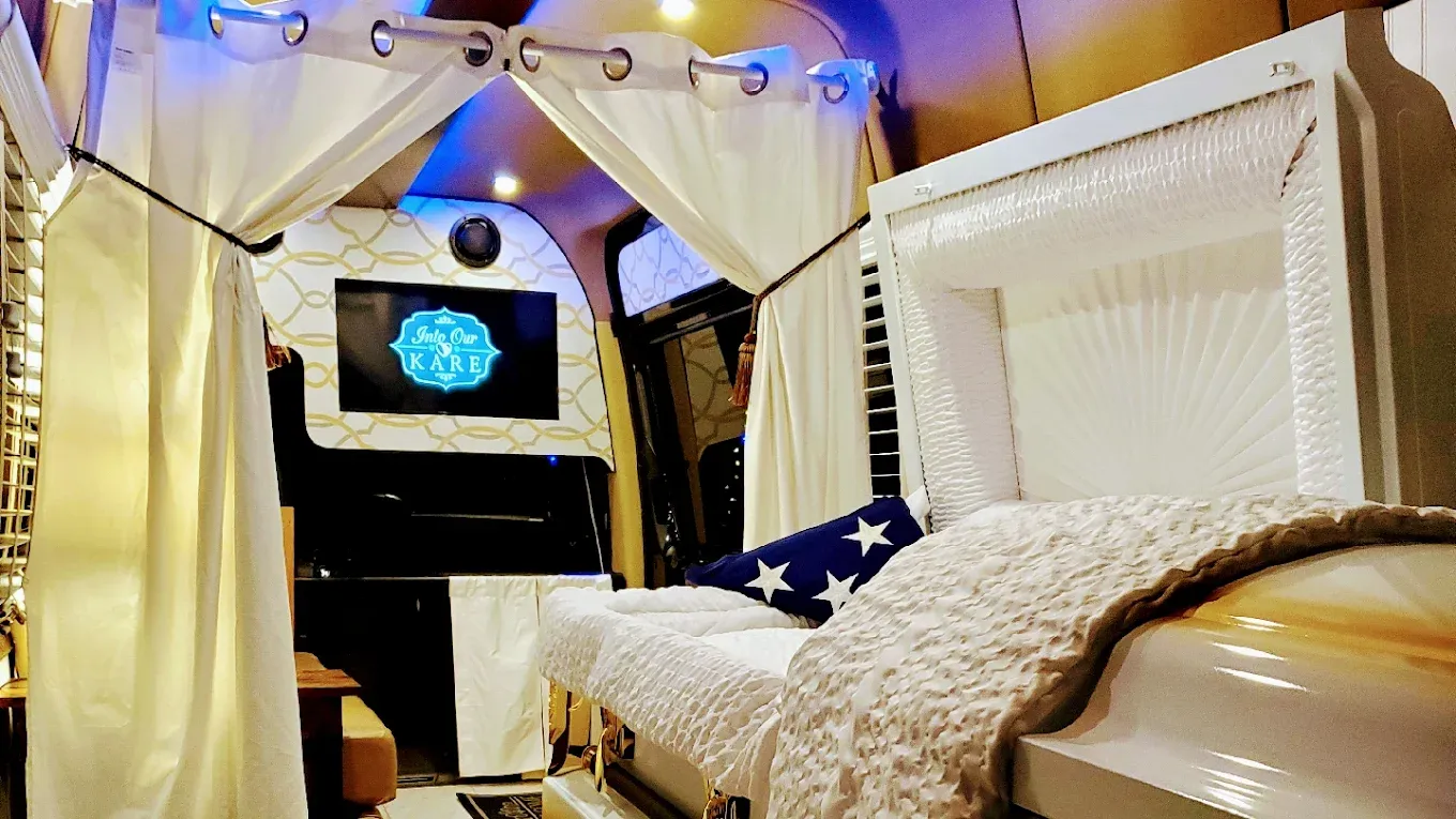 Interior of a cozy white camper van with a bed, string lights, and a small screen at the back.