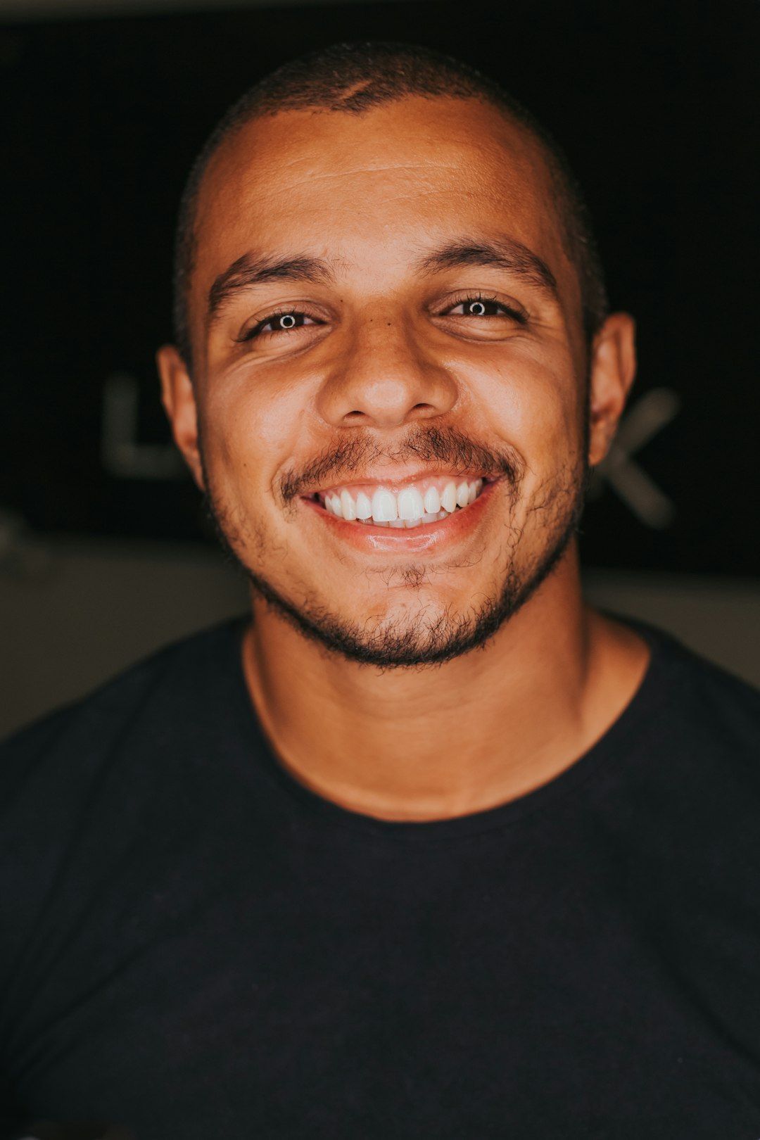 Smiling man with brown skin and a shaved head in a black shirt.