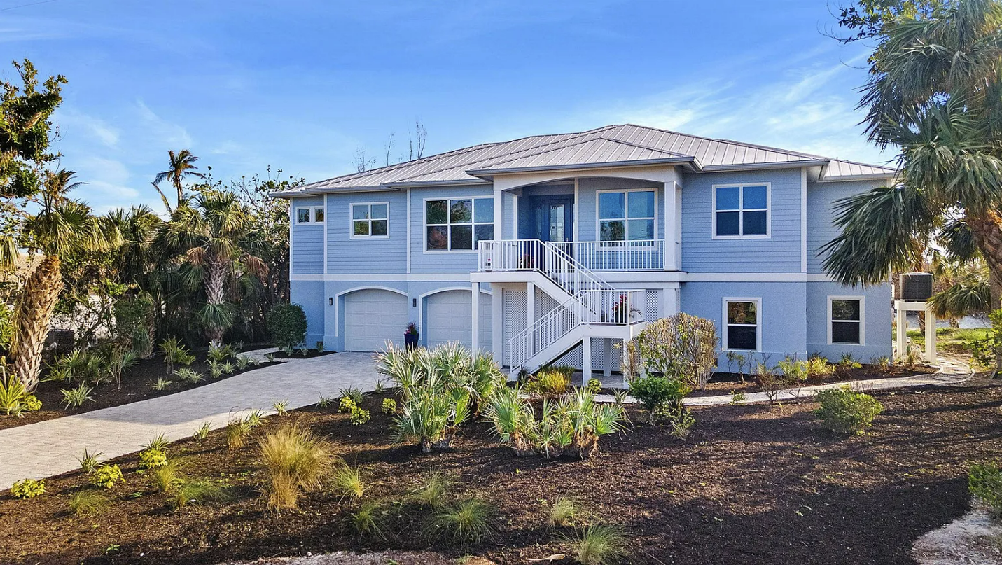 A large blue house with a lot of windows is surrounded by trees and bushes.