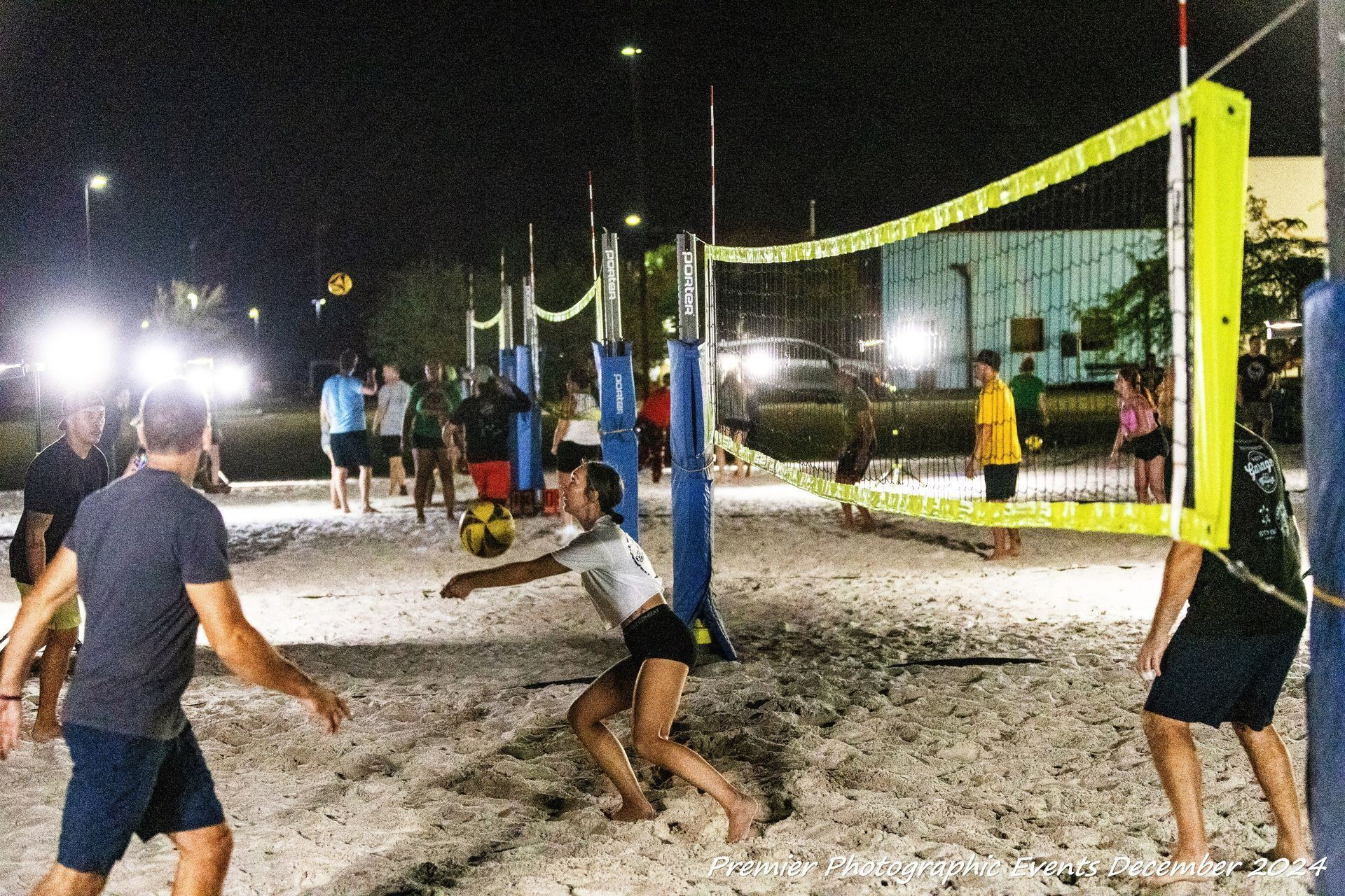 Beach volleyball game at night, players hitting the ball, under bright lights.