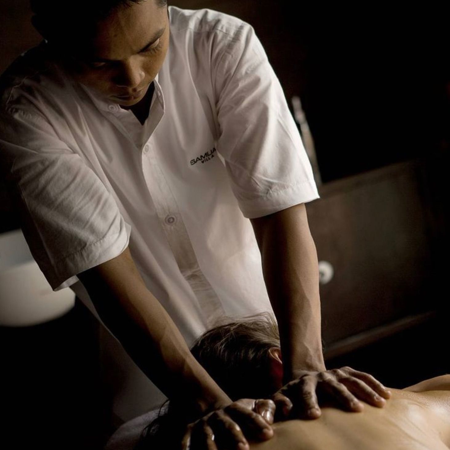 Massage therapist giving a back massage in a dimly lit spa room