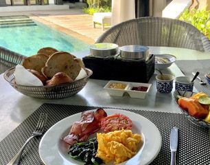 Complimentary Breakfast by a pool, with eggs, bacon, fruit, and bread in woven baskets.