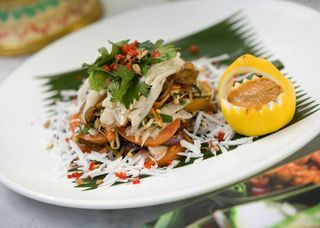 Plated salad with shredded vegetables, herbs, and a lemon half on a white dish