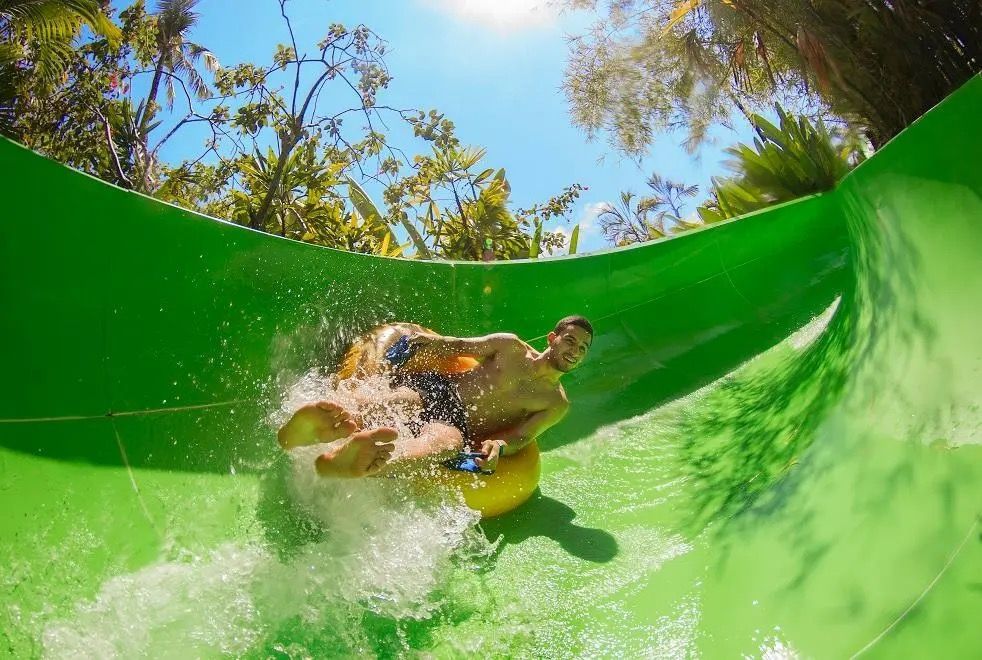 Person sliding down a bright green water slide with splashing water and blue sky above