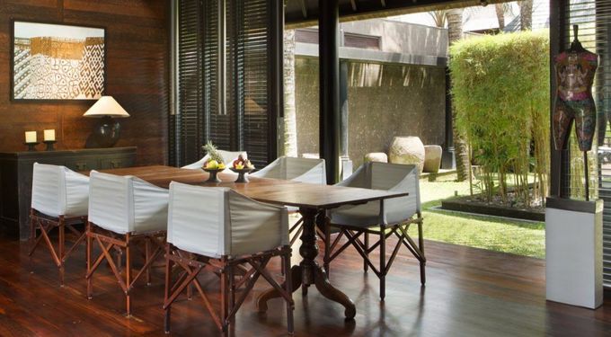 Modern dining room with glass walls, wooden table, white chairs, and a view of a patio and garden