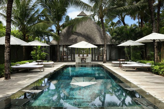 Tropical resort pool with white umbrellas, lounge chairs, and palm trees reflected in the water