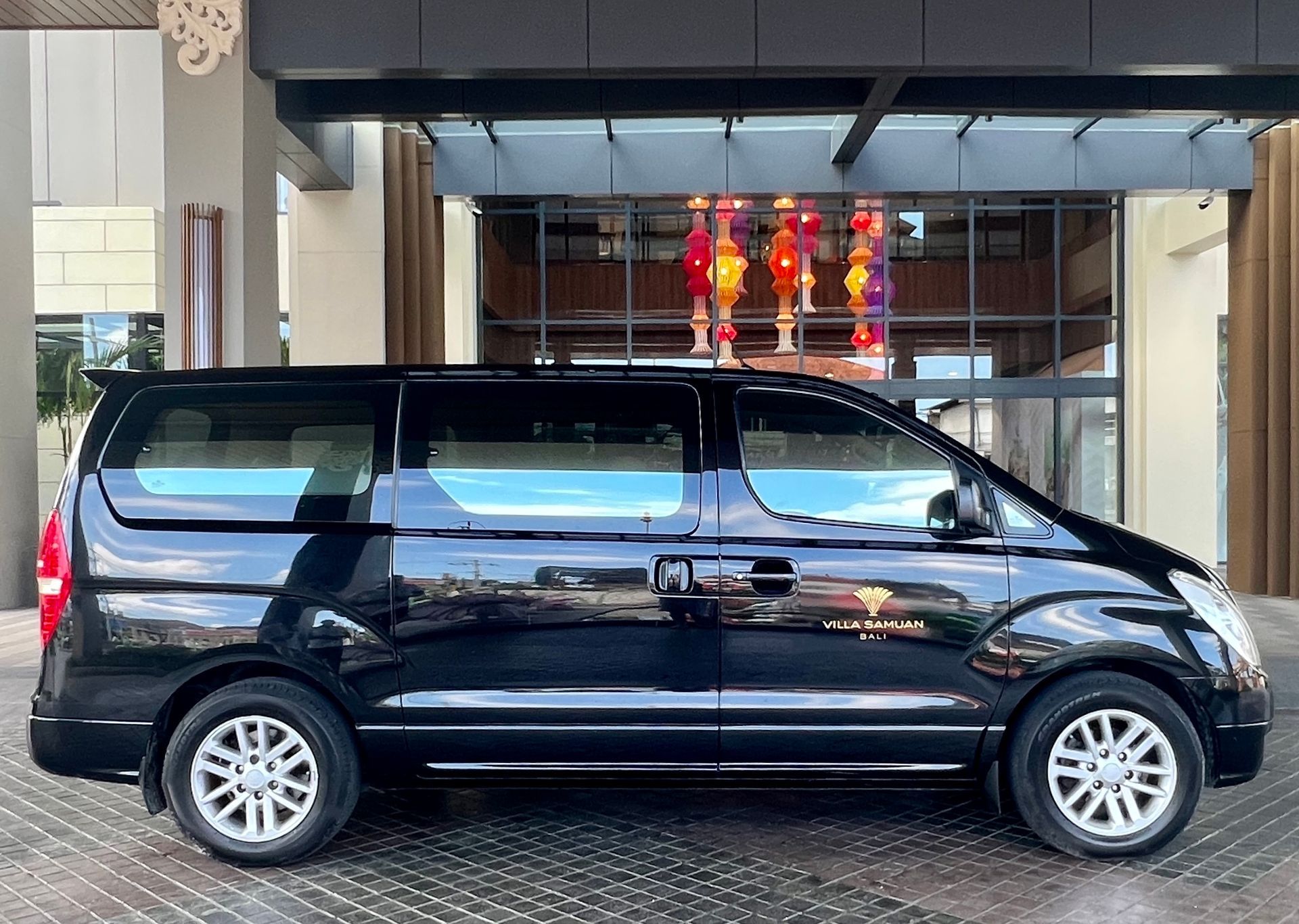 Black minivan parked at a hotel entrance under a covered driveway with glass doors behind.