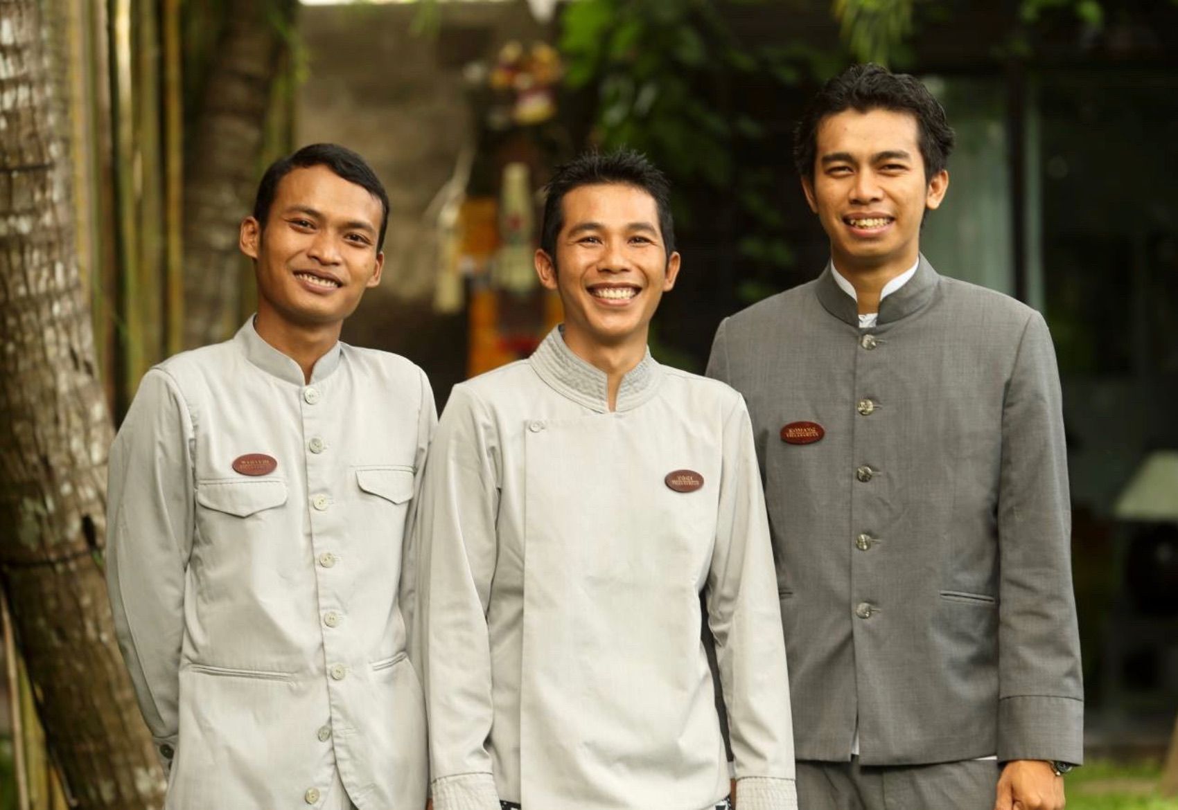 Three men in traditional light-colored outfits standing outdoors and smiling