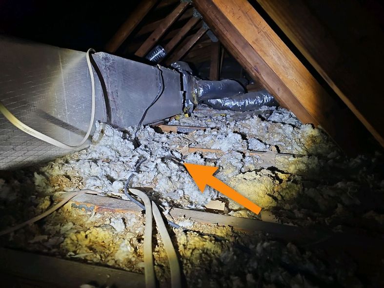 Damaged attic insulation and ductwork, with debris and an orange arrow pointing to the problem area.