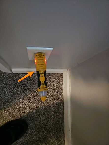 Yellow caulk tube in a wall-mounted dispenser above speckled flooring, with an orange arrow pointing to it