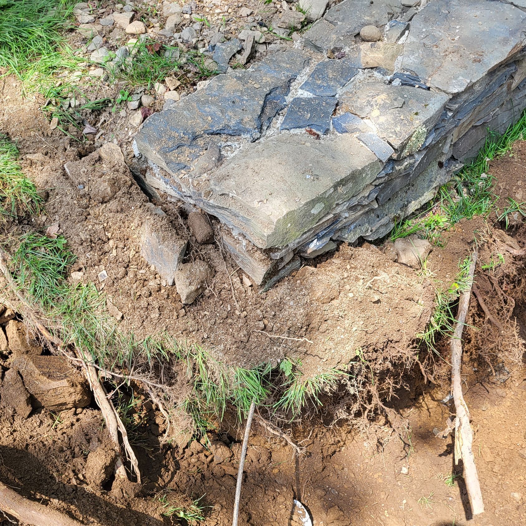 A large rock is sitting on top of a pile of dirt and grass.