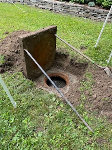 A manhole cover is sitting in the grass next to a hole in the ground.