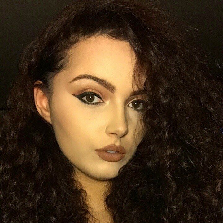A woman with long curly hair is taking a selfie.