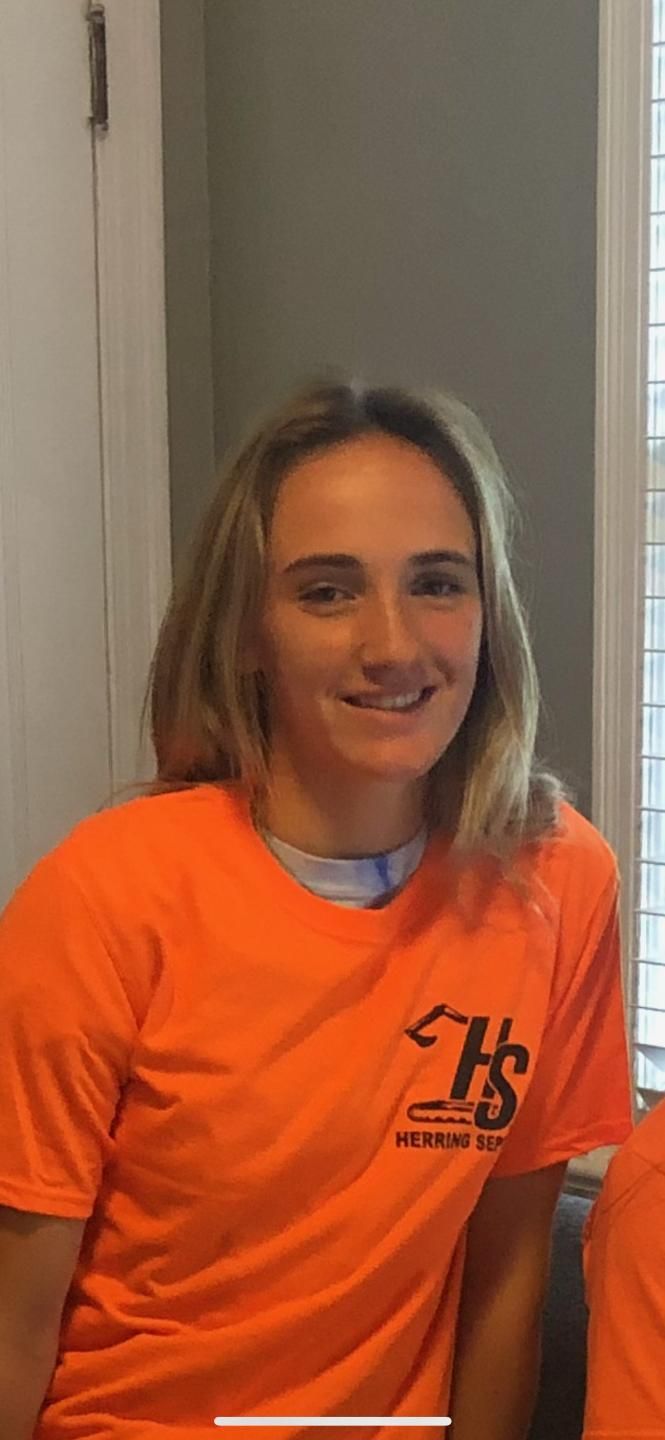 A woman is wearing an orange t-shirt and smiling.