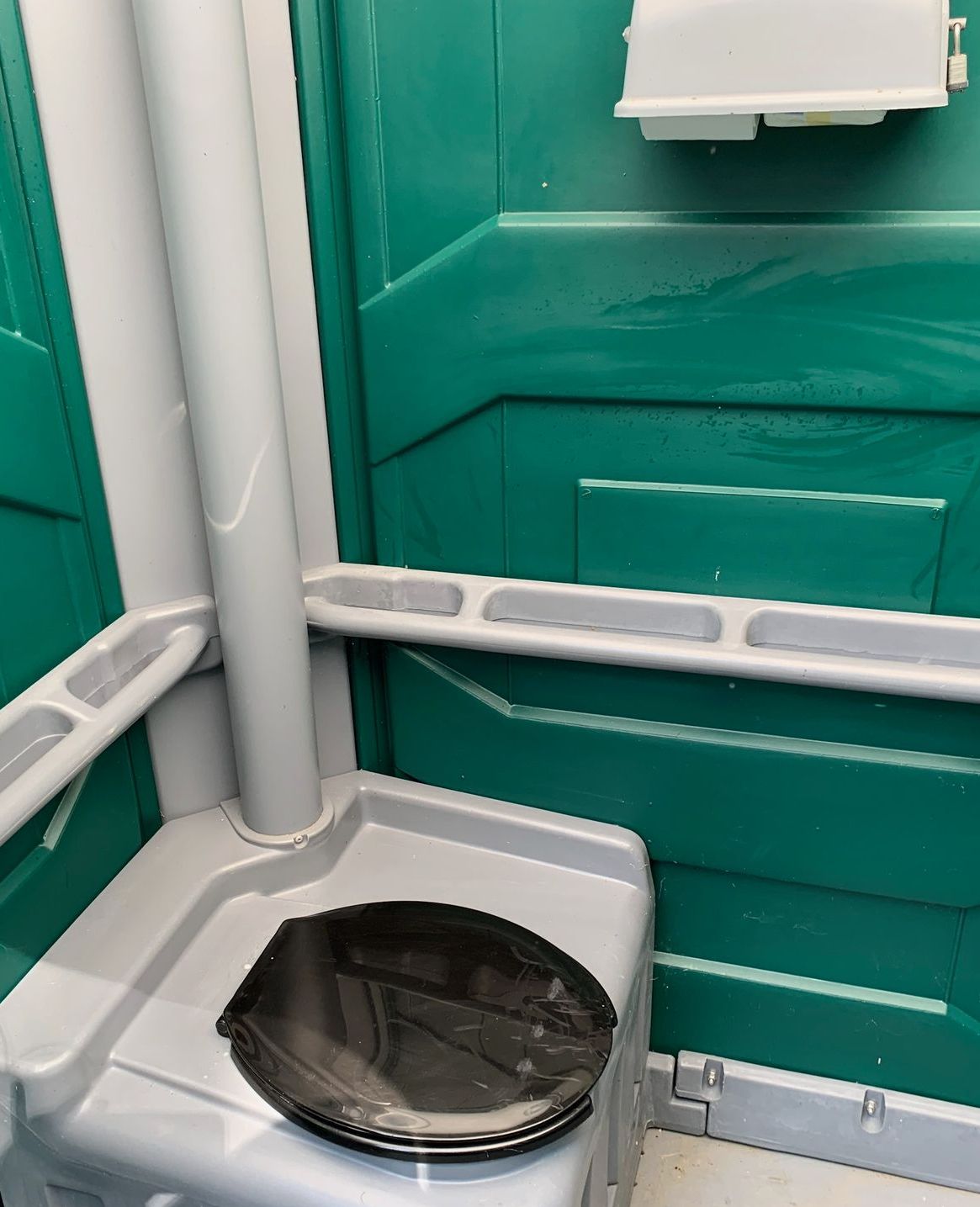 A portable toilet in a green bathroom with a trash can on the floor.