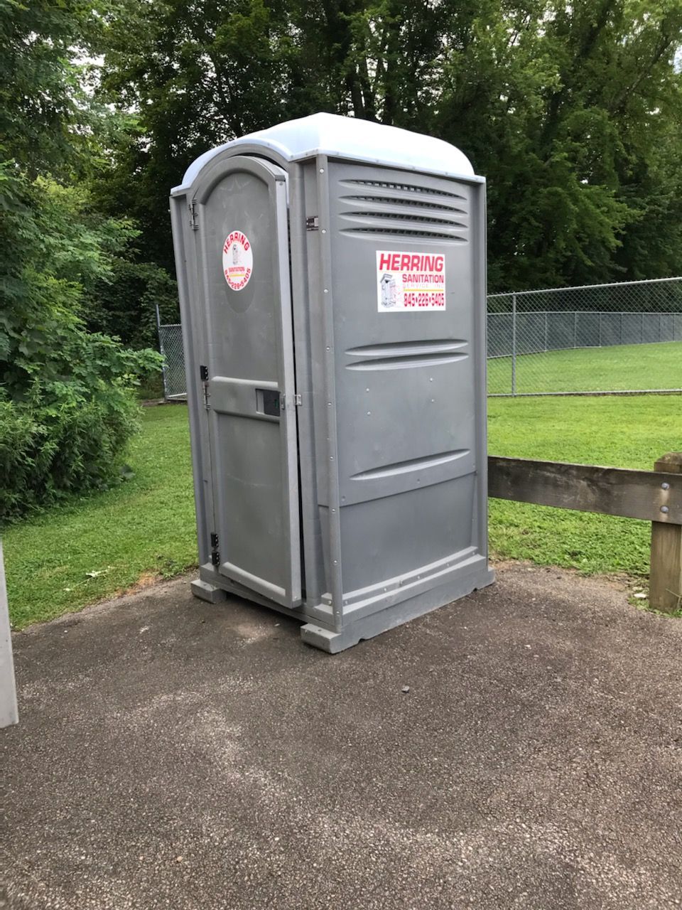 A portable toilet is sitting on a sidewalk next to a fence.