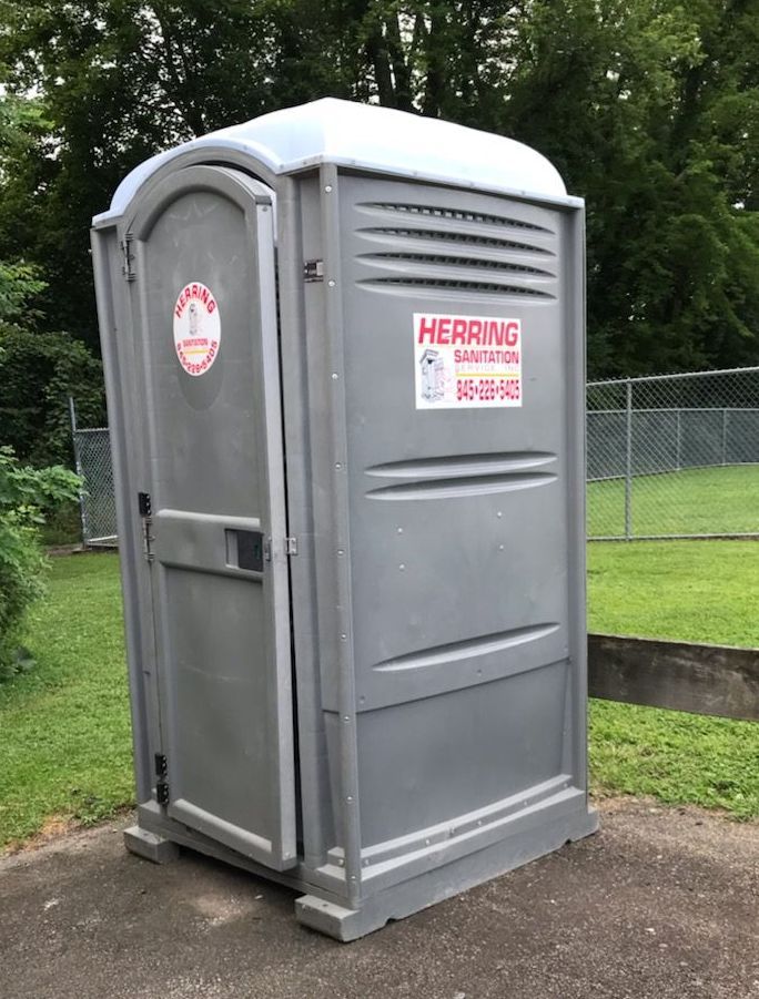 A portable toilet is sitting on the side of the road next to a fence.