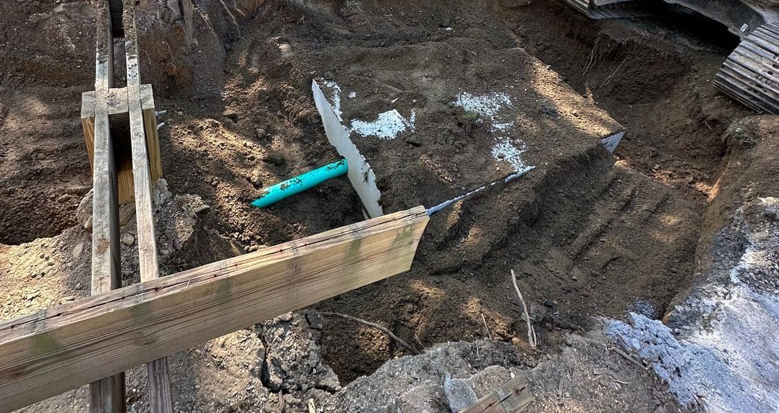 A person is using a chainsaw to cut a piece of wood in the dirt.