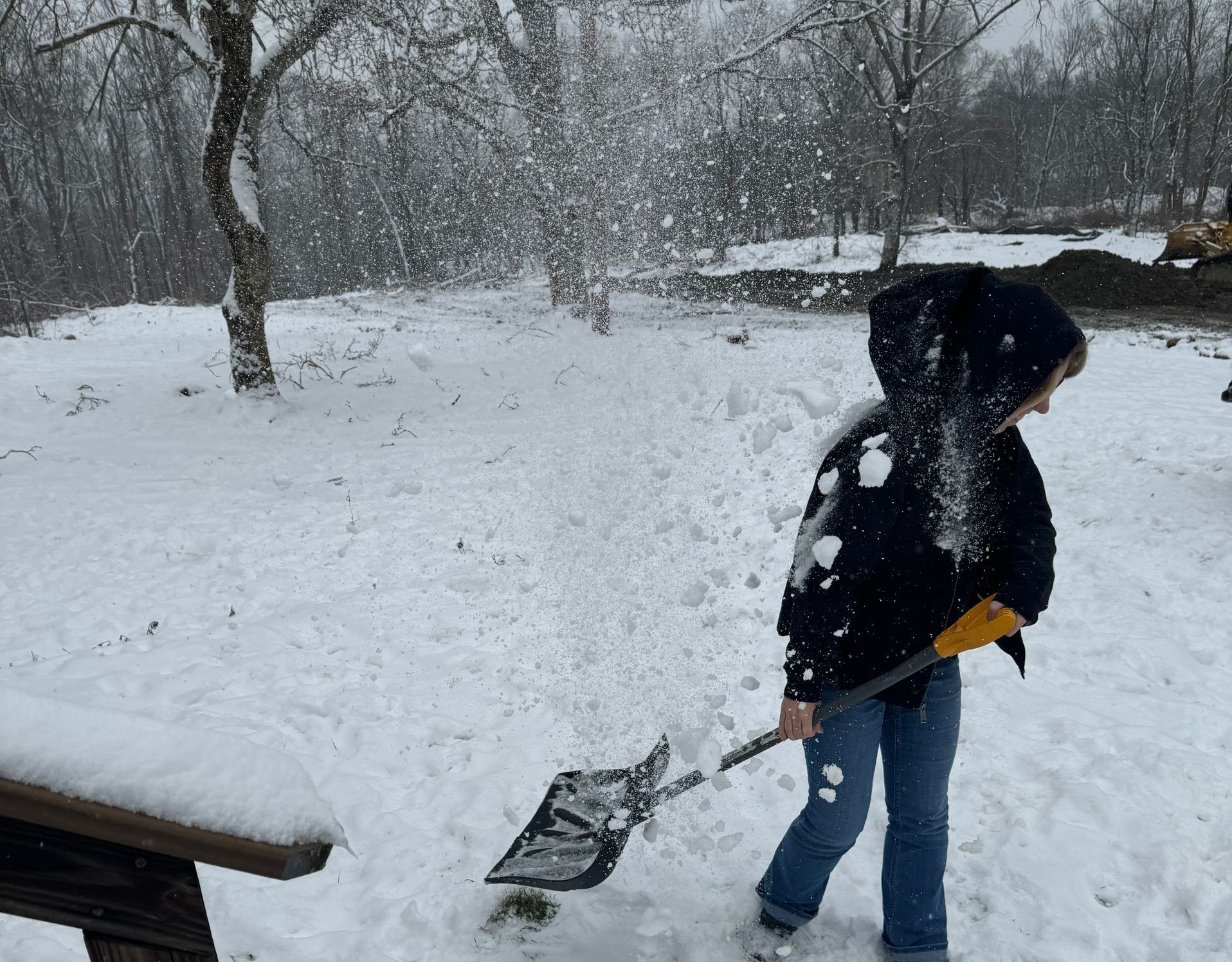 A person is shoveling snow in front of a picnic table