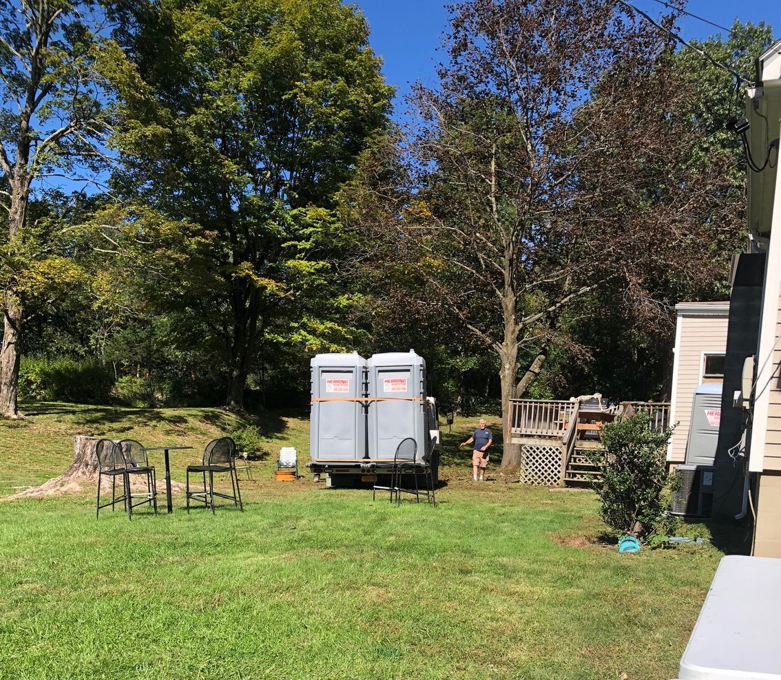 A couple of portable toilets are parked in the grass in front of a house.