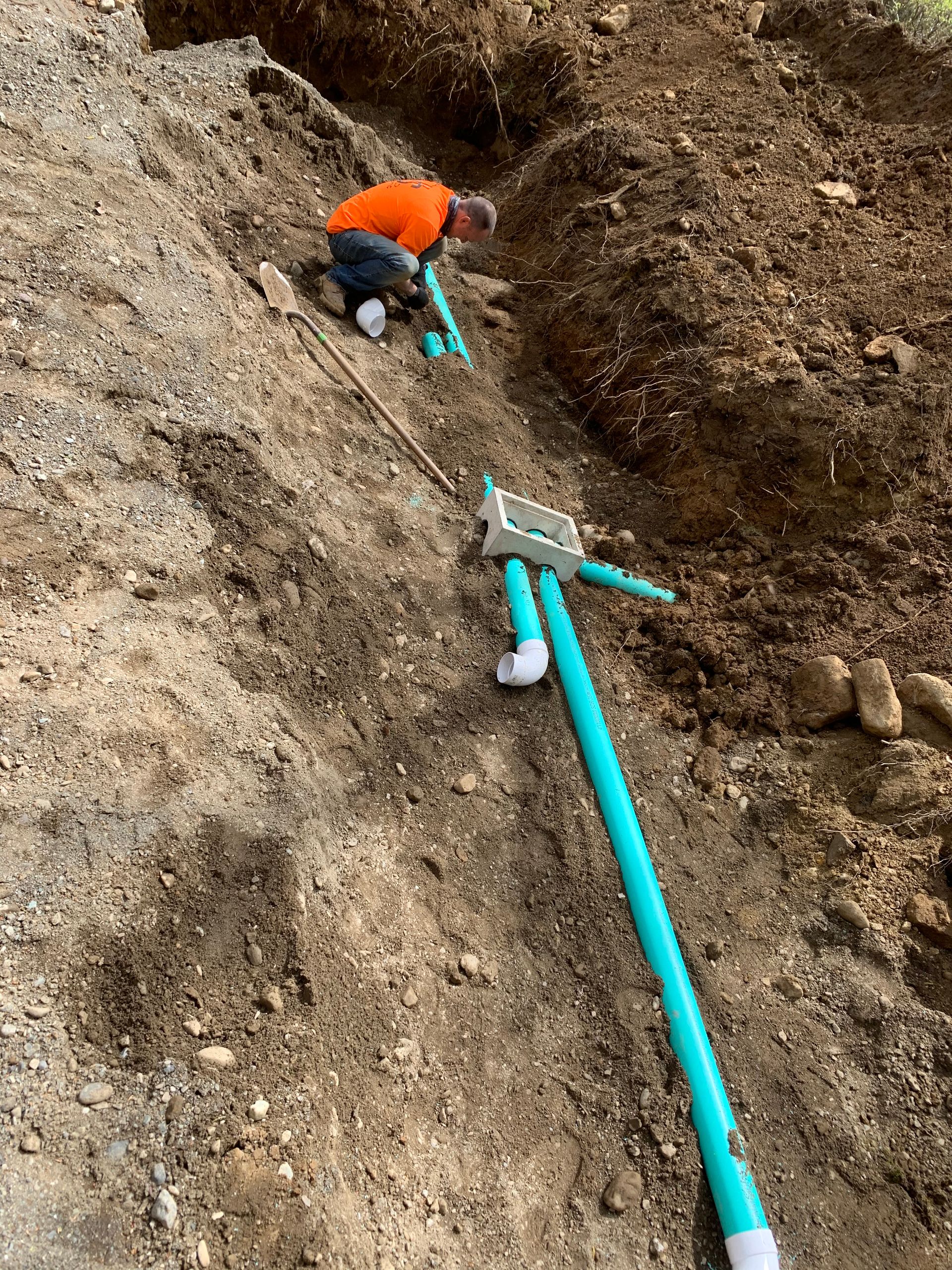 A man is working on a pipe in the dirt.