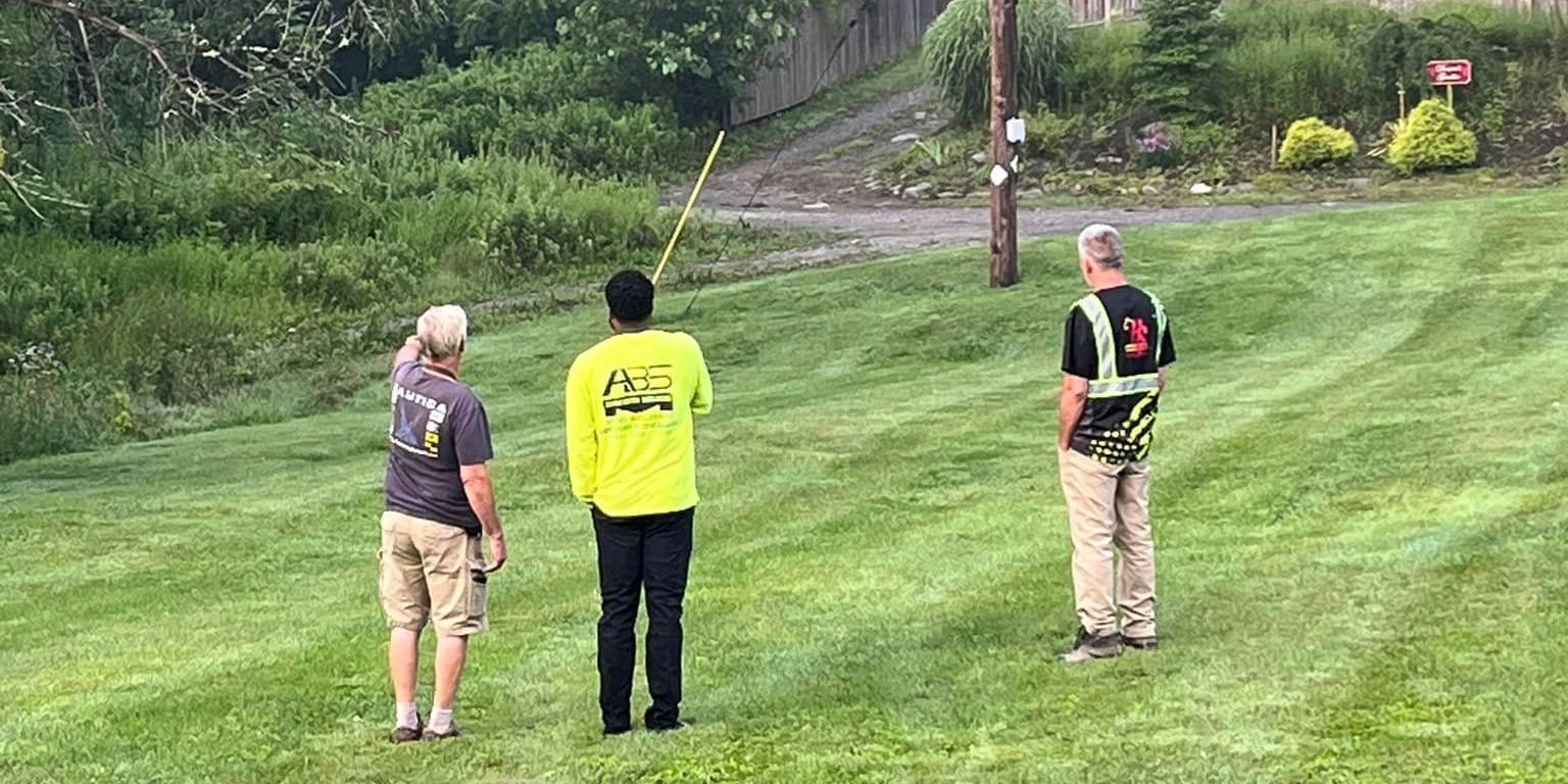 Three men are standing in a grassy field looking at something.
