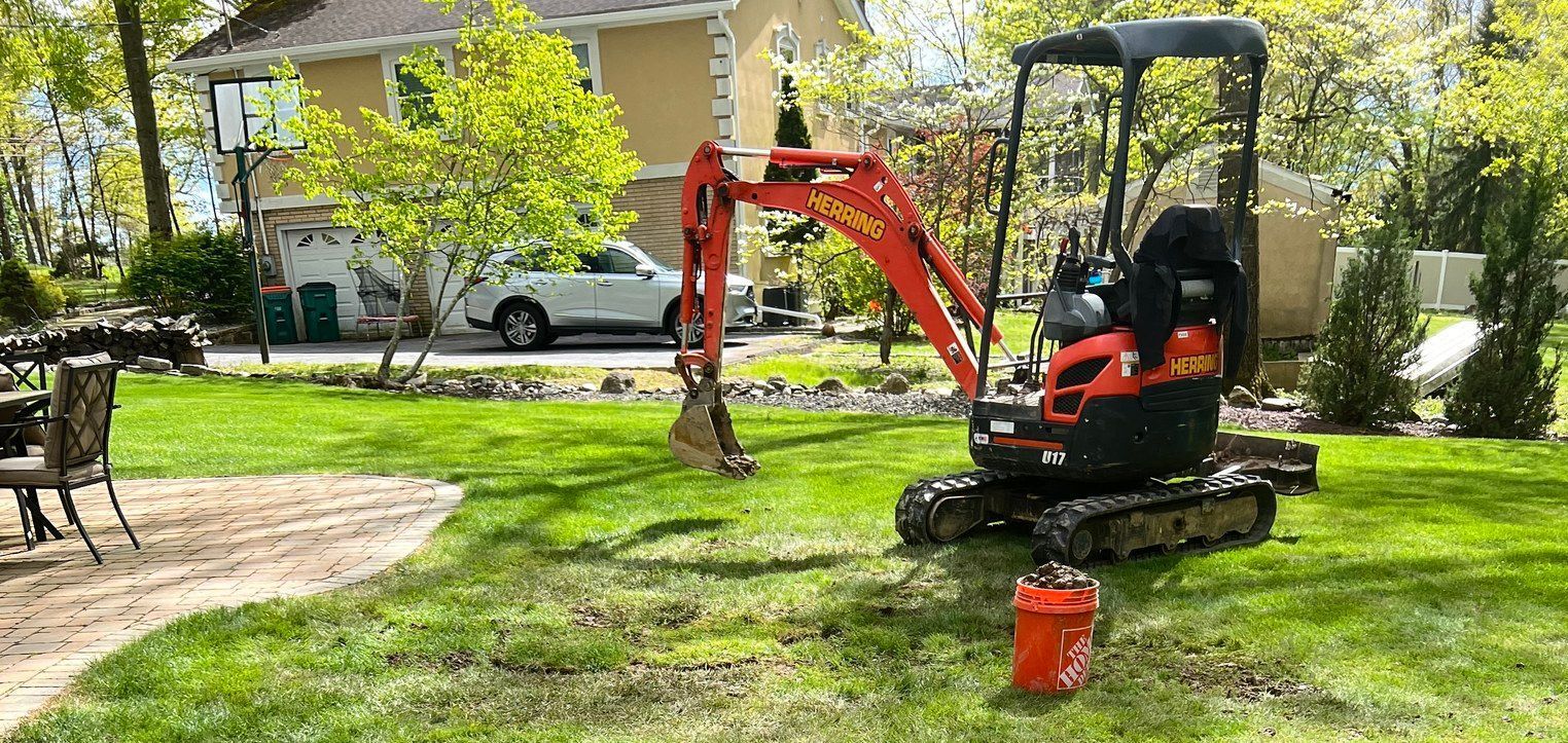 A small excavator is sitting in a lush green yard next to a house.