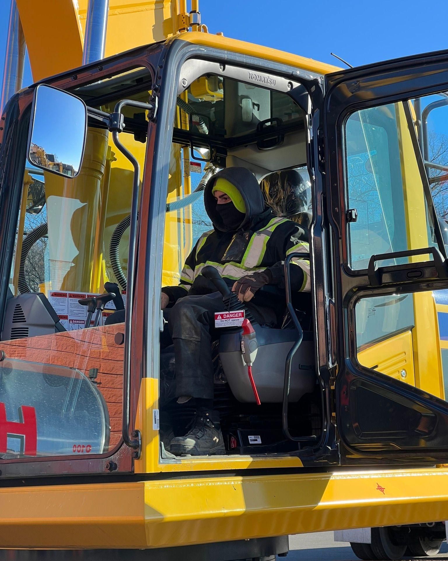 A man is sitting in the driver 's seat of a yellow excavator.