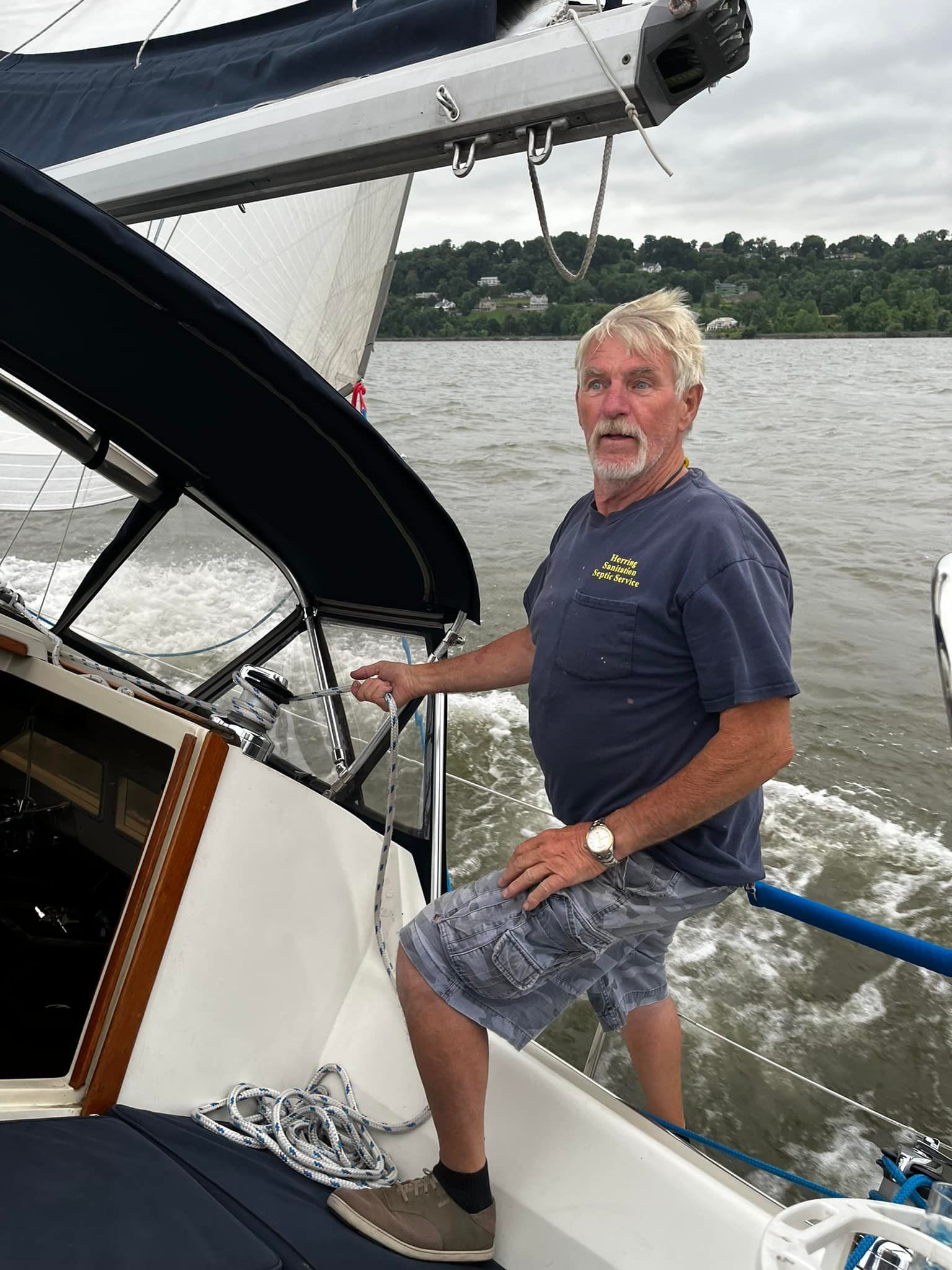 A man is sitting on the side of a sailboat in the water.