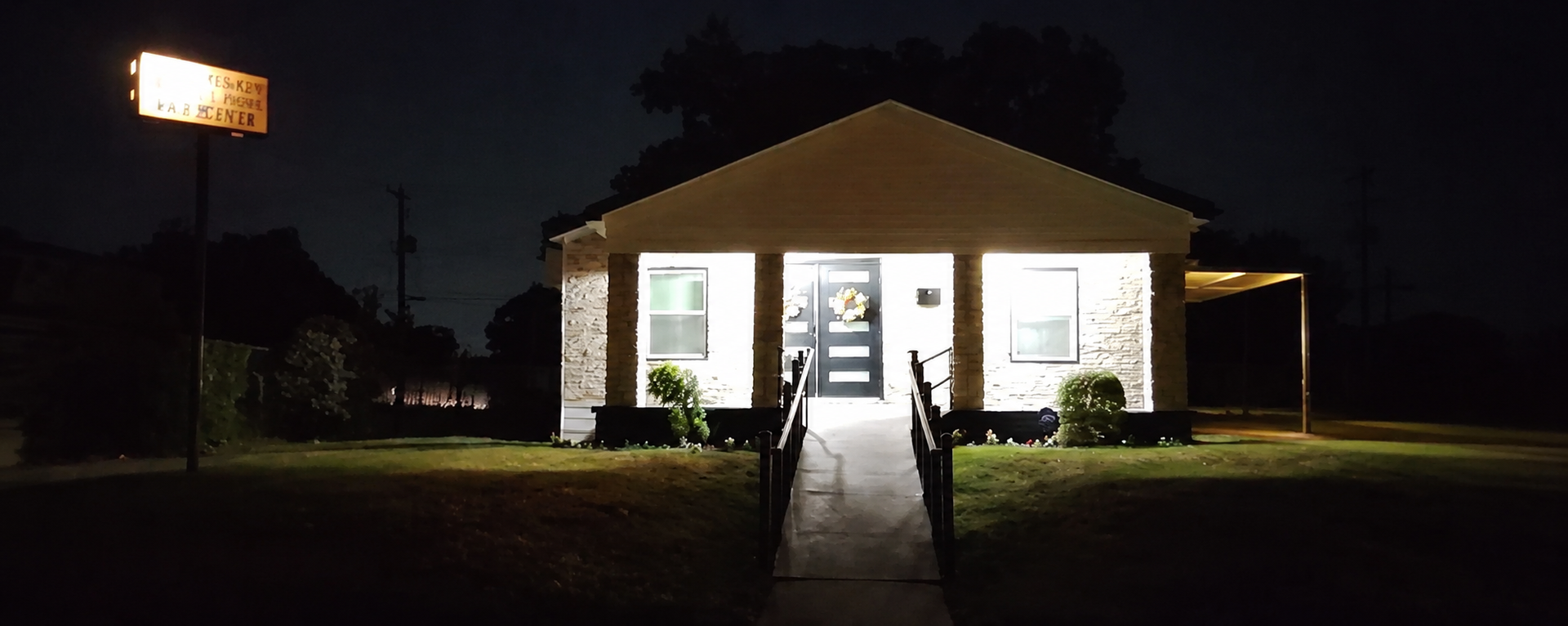 Nighttime view of a lit storefront with a ramp leading to the entrance and a glowing sign to the left