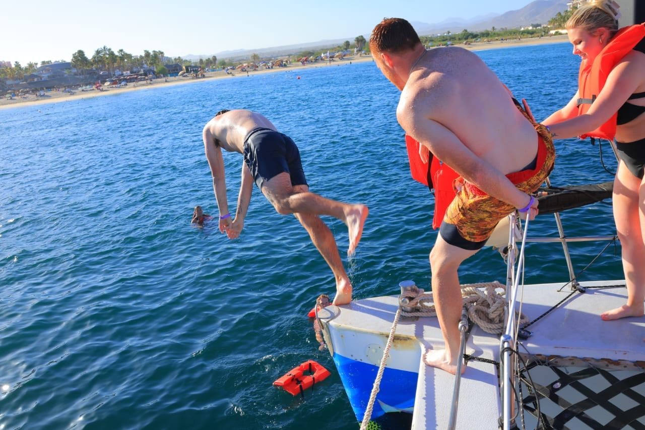 Two people jump off a boat into clear blue water on a sunny day.
