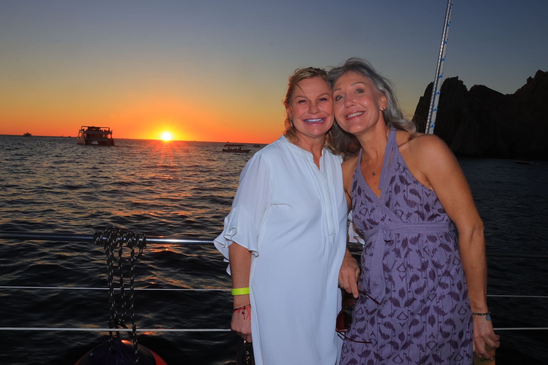 Two women are posing for a picture on a boat at sunset.