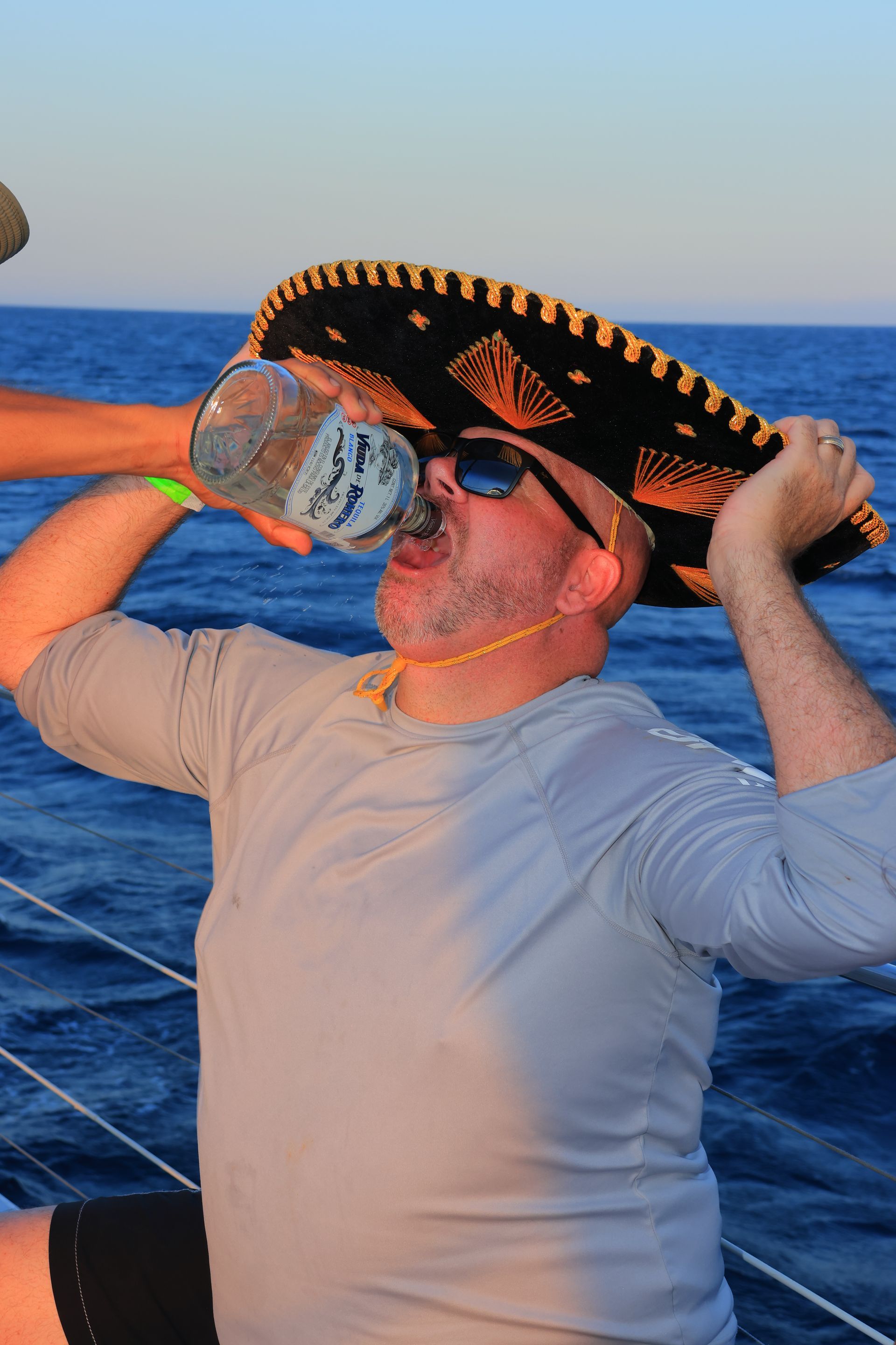 Person on a boat holds a sombrero over their face with the ocean behind them