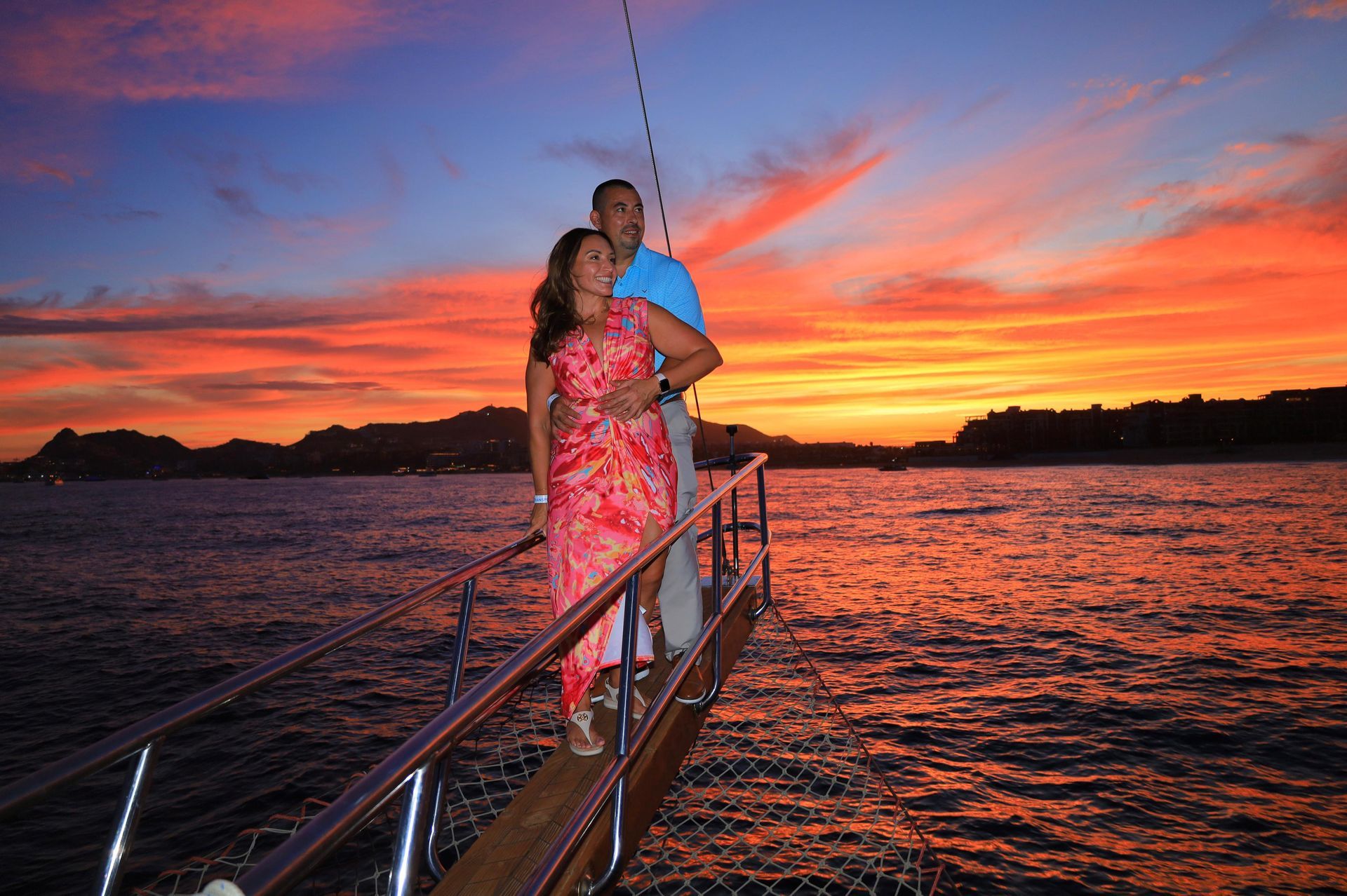 A man and a woman are standing on a boat at sunset.