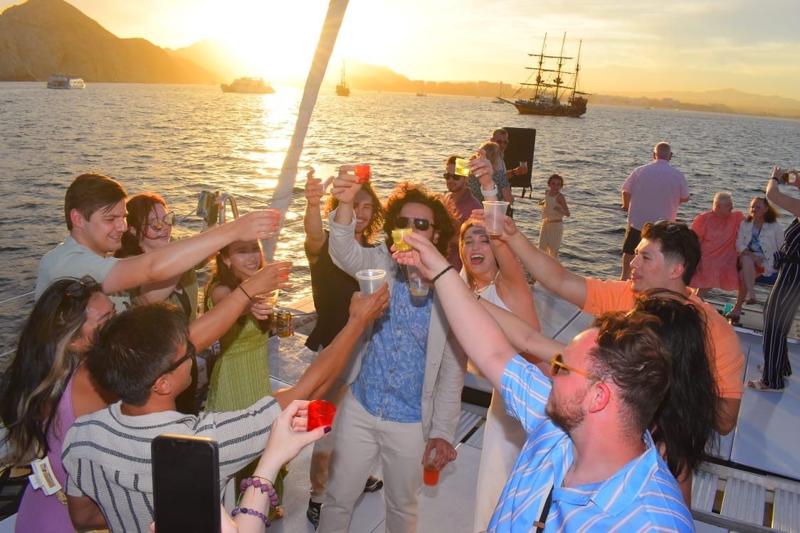 People toasting drinks on a boat deck at sunset by the water