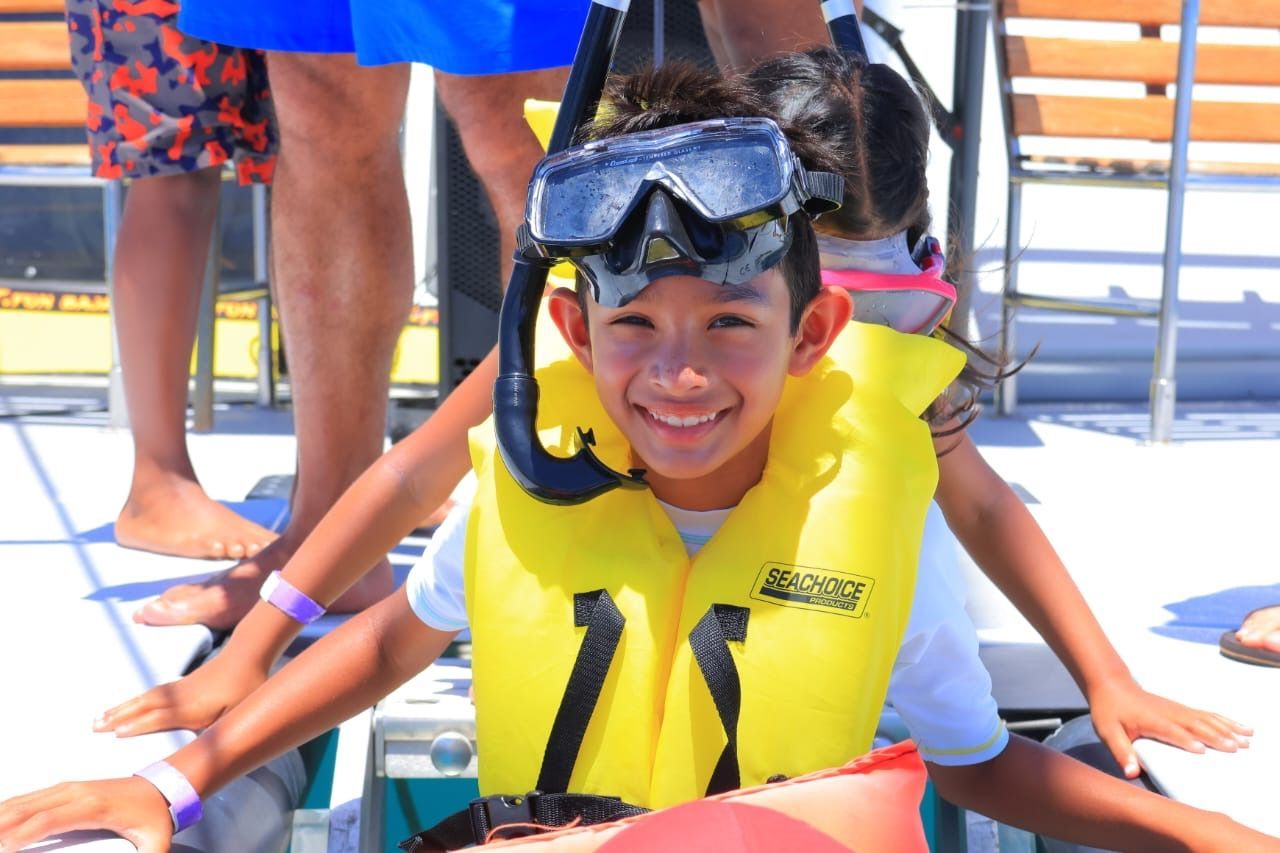 Child smiling in a yellow life jacket and snorkel mask on a boat, with people standing behind them