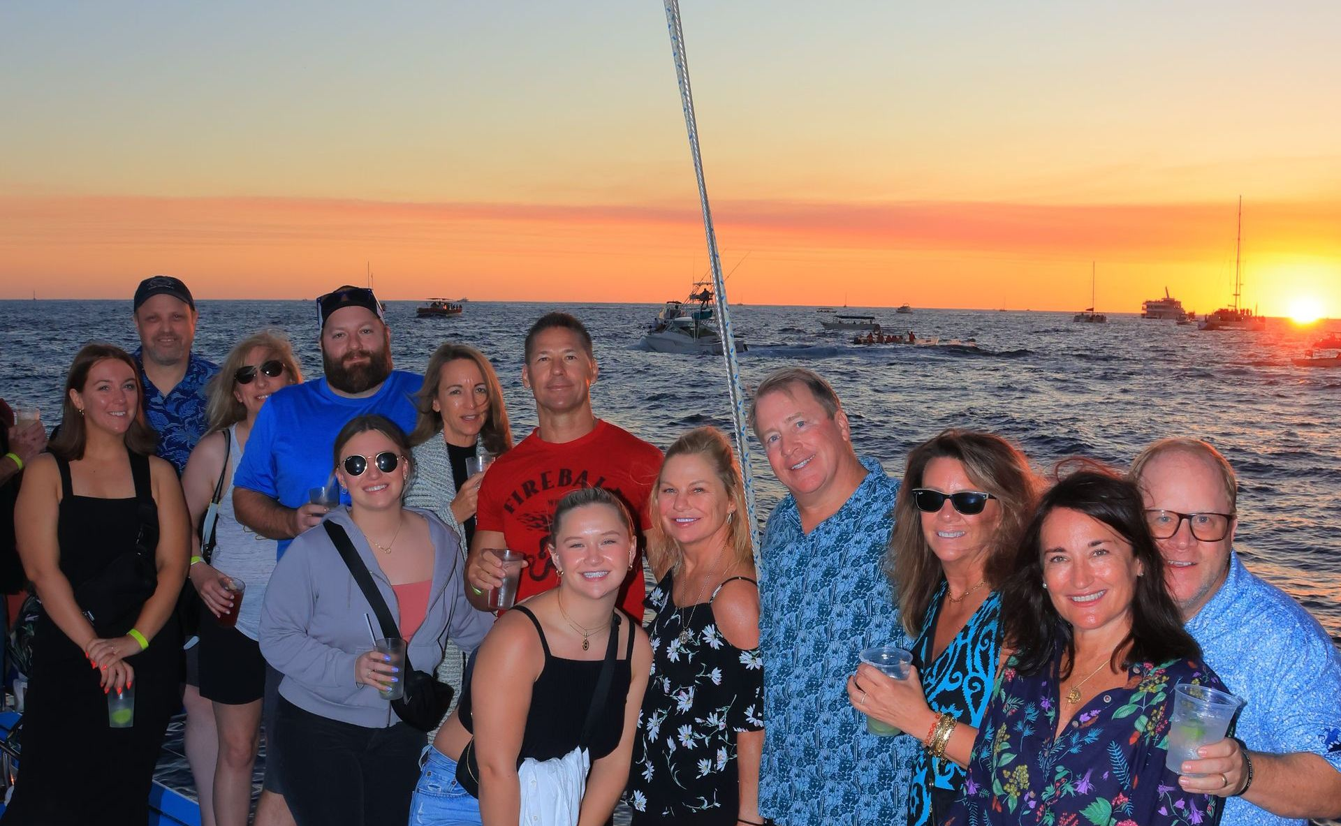 Snorkel Tours Cabo San Lucas Group of friends on a boat deck at sunset, smiling with ocean and orange sky behind them.