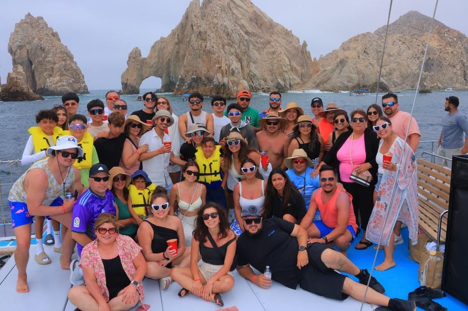 Group of people posing on a boat deck with blue water and rocky coastal cliffs in the background