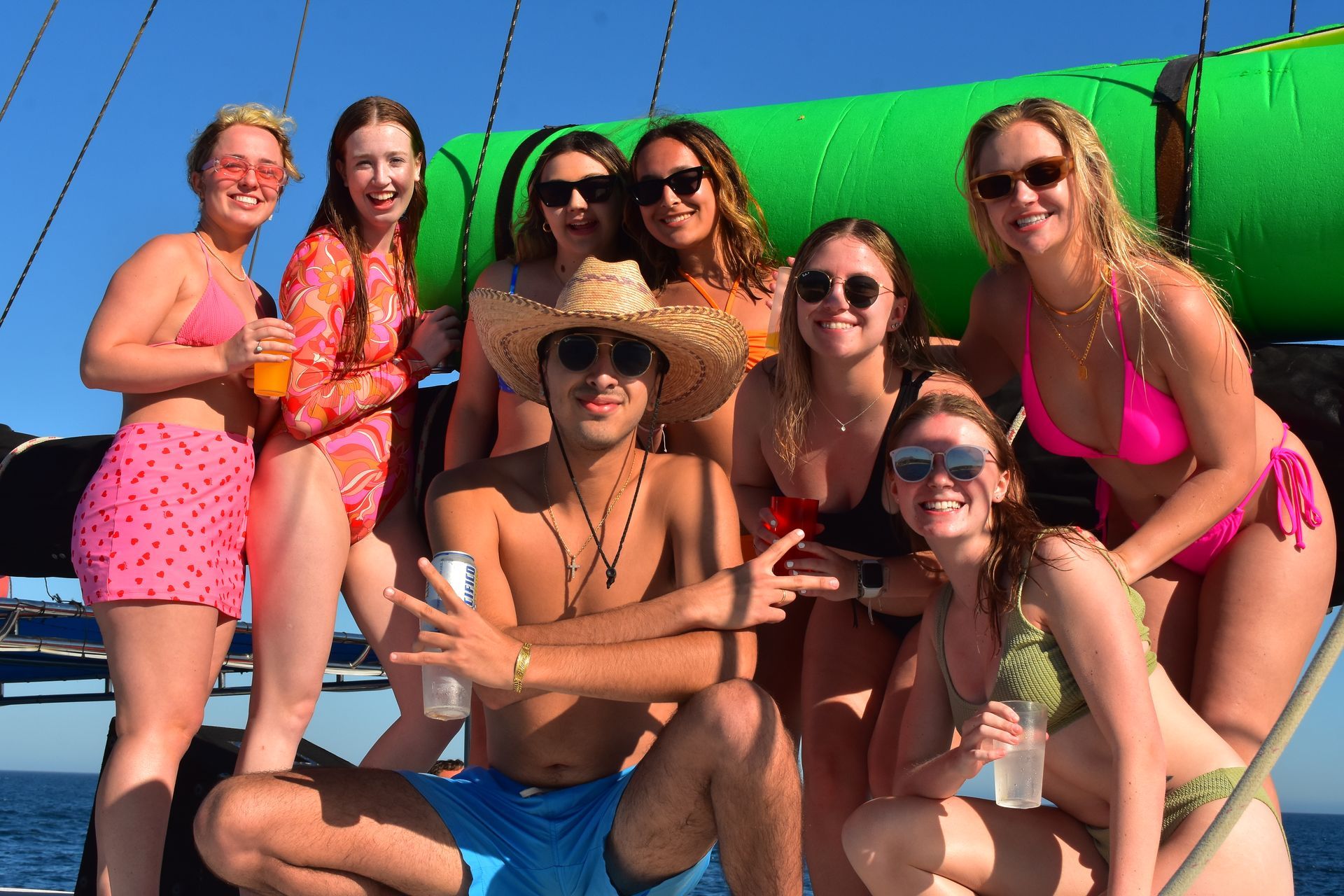 Group of friends posing on a boat deck in bright swimsuits and sunglasses under a clear blue sky.