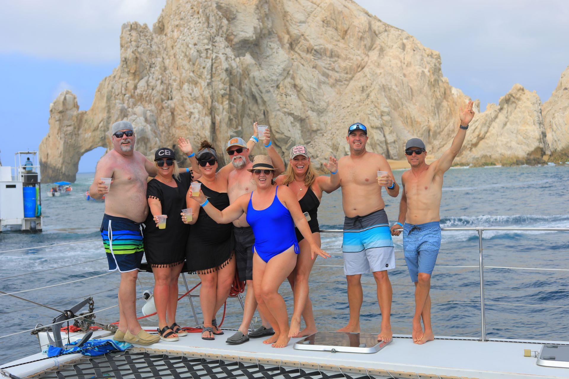 Group of people posing on a boat deck in front of a rocky seaside cliff.