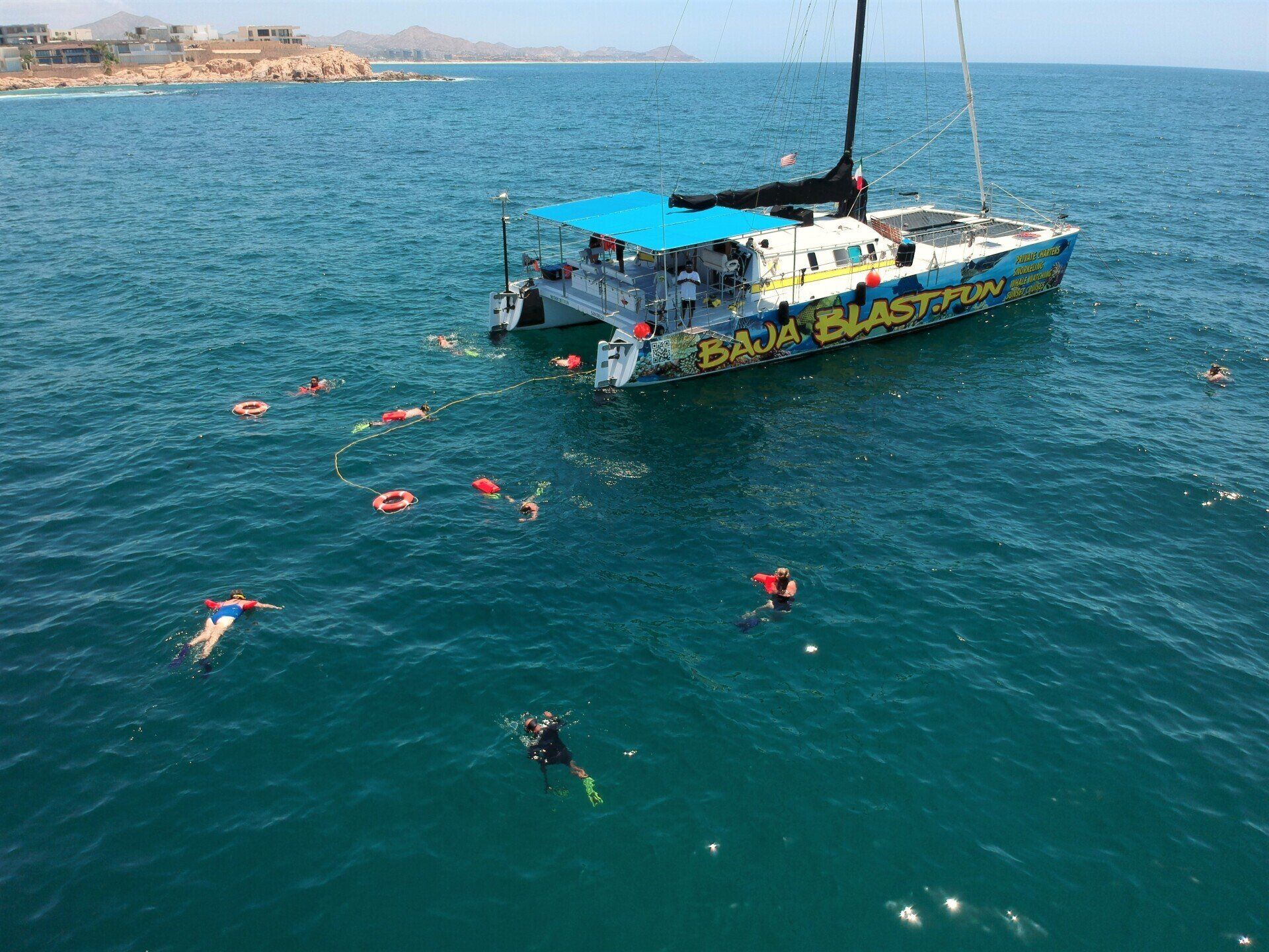 Snorkelers swim around a colorful boat in clear blue ocean near a rocky coastline.