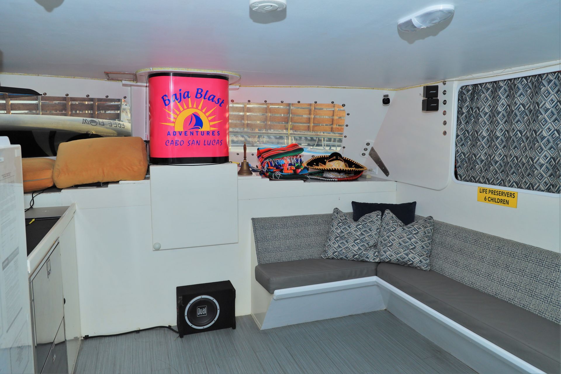 Modern boat cabin with white walls, gray bench seating, and a bright red TV screen above storage shelves