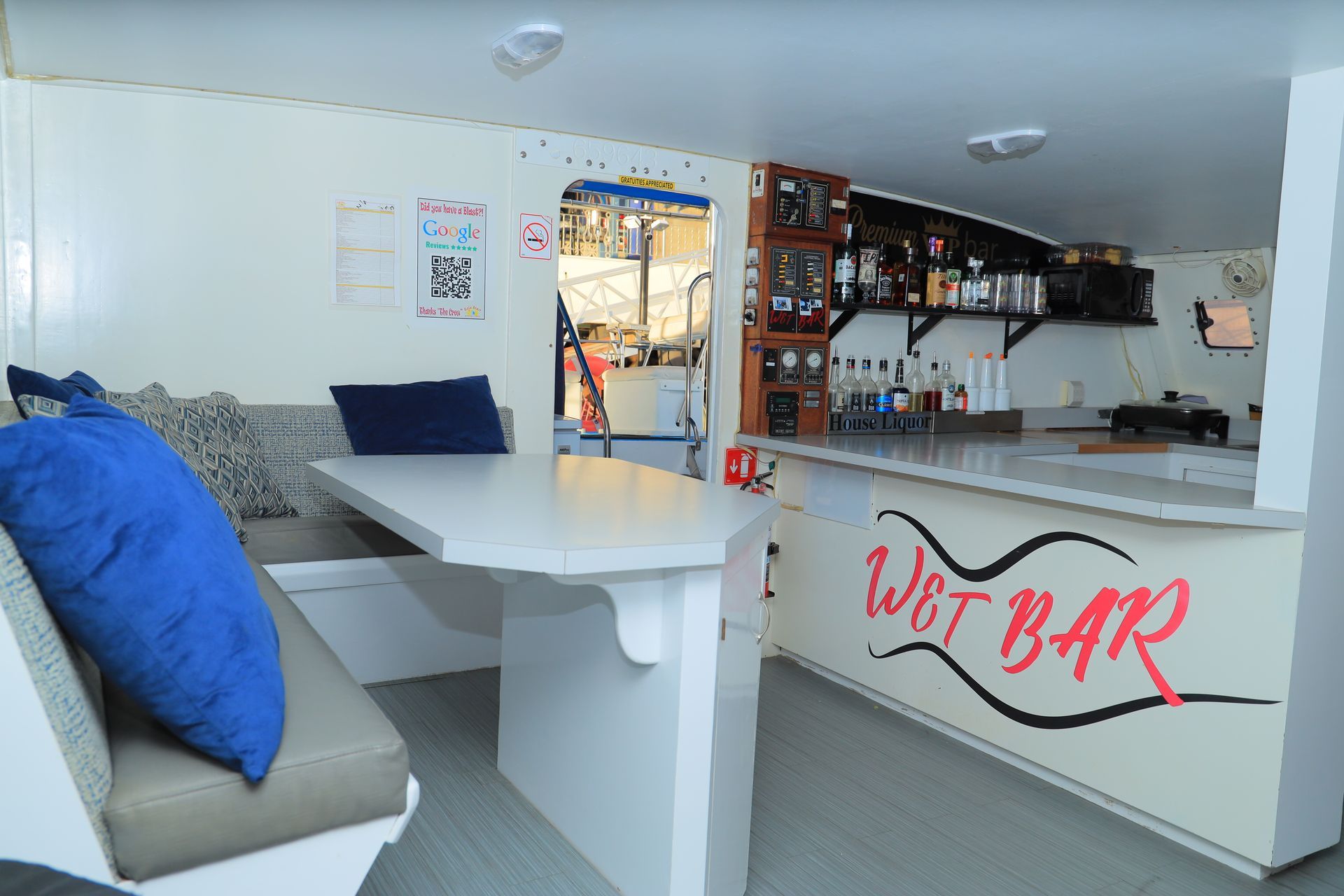White bar interior with a counter, tables, blue cushions, and shelves of bottles behind the bar.