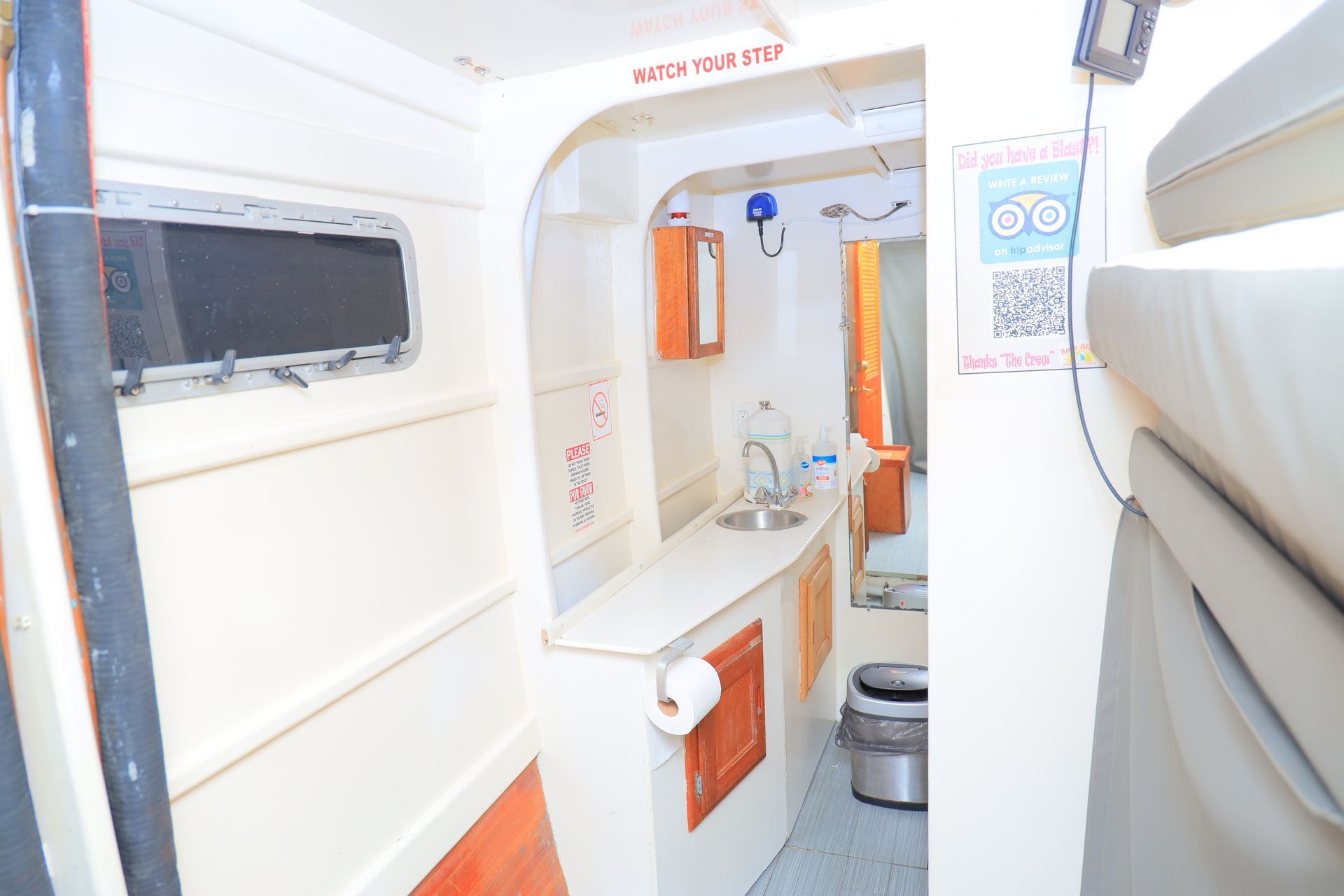 Narrow white bathroom in a camper or boat with sink, mirror, toilet, and shower curtain