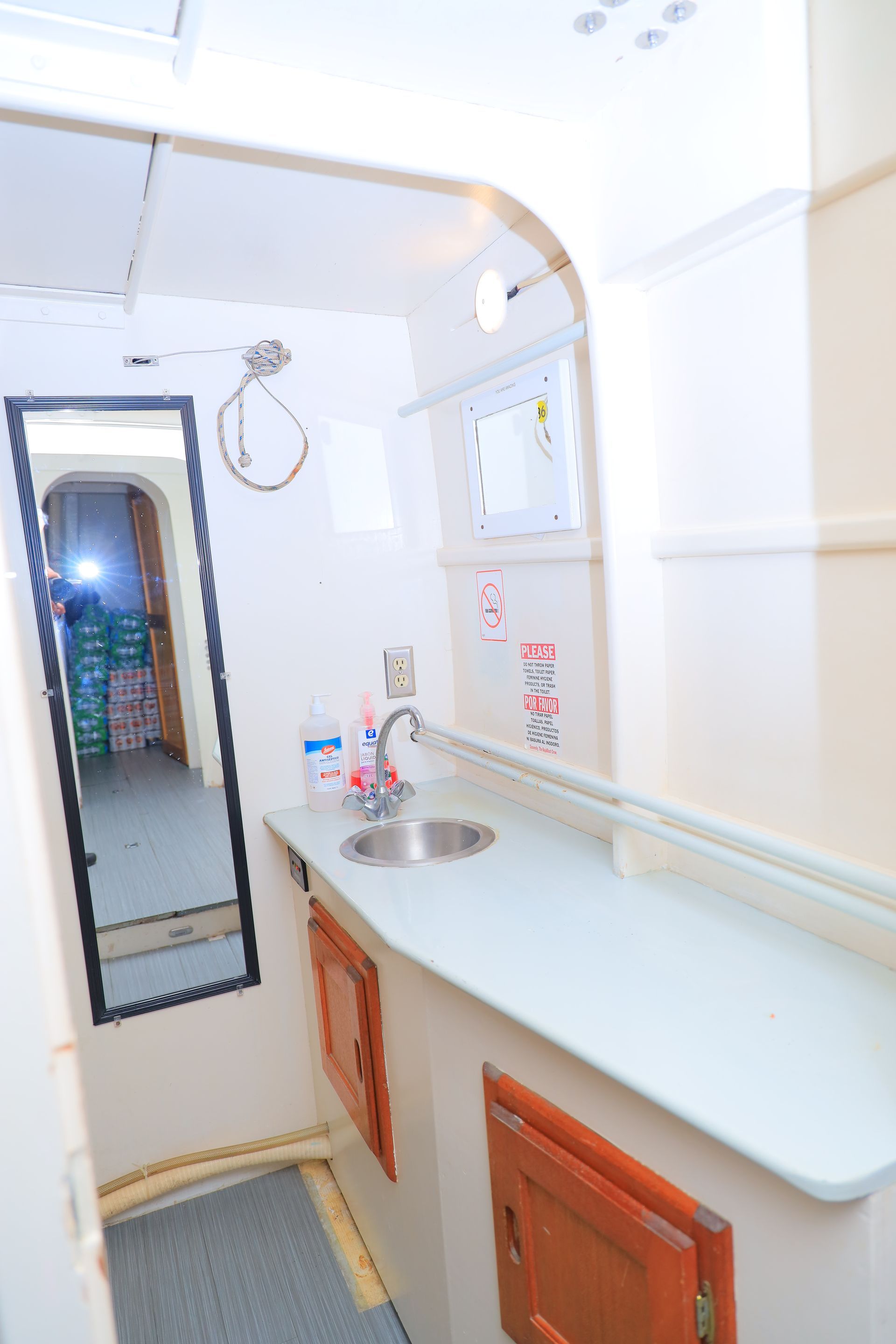 Narrow kitchenette with white counters, sink, mirror, cabinets, and wall-mounted water heater.